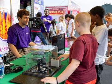 Two fifth grade students look at world's smallest fidget spinner at table with ORNL scientist