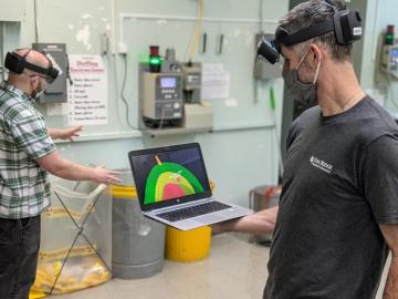 ORNL inventor Michael Smith, right, holds a laptop showing what Scott Greenwood, left, sees through an augmented reality headset. 