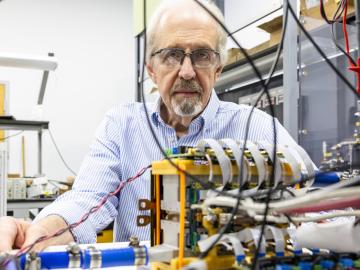 Scientist is in his lab with wires and electronics in the foreground, one with a medium yellow box. 