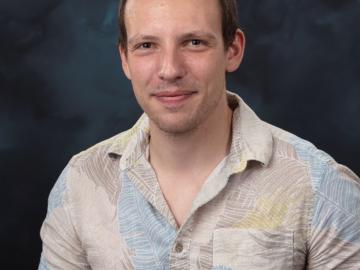Profile photo of man in short sleeve button up shirt with blue and grey feather pattern. 