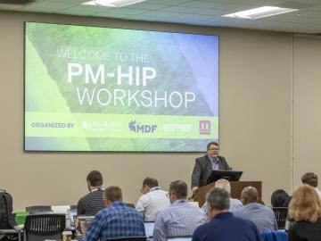 A speaker is standing at the podium in front of a PowerPoint slide with the title of the workshop on it, with 10 people in the audience