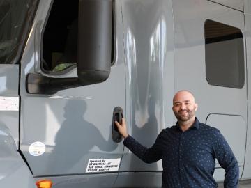 Man is standing outside of a grey semi-truck posing for a photo