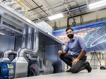 Researcher Maximiliano Ferrari is kneeling down next to an emulator in the networked microgrids laboratory at the Grid Research Integration and Deployment Center