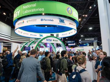 Wide shot of the expo center, ground filled with people walking and a green, white and blue 3D circle sign above everyone in the center