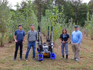 Four scientists are standing in a field next to a data-gathering tool robot
