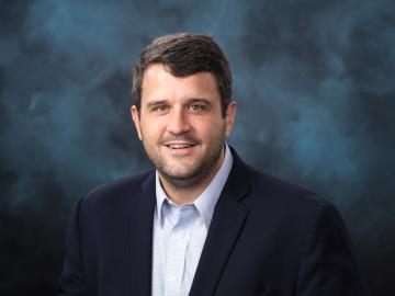 ORNL chemist Benjamin Manard is posing for a photo with a light blue and navy background