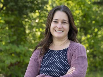 ORNL researcher Melissa Cregger is standing outside smiling for a photo. Woman is wearing blue and white polka dot shirt with a purple cardigan. 