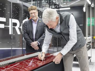 Secretary Wright leans over red computer door, signing with silver sharpie as ORNL Director Stephen Streiffer looks on