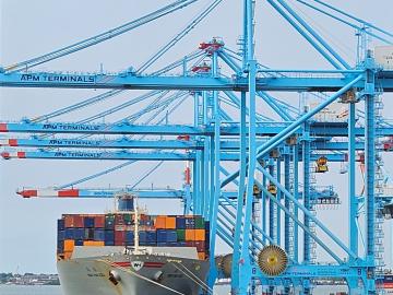 A cargo ship to the left of the seaport with bright blue metal surrounding it