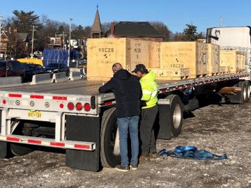 Two men are talking on the backside of a semi trailer holding big wooden boxes