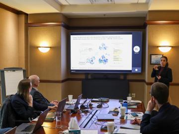 Erica Prates is presenting to a group of attendees at Vandy workshop in a table conference room, standing next to a screen glowing in white