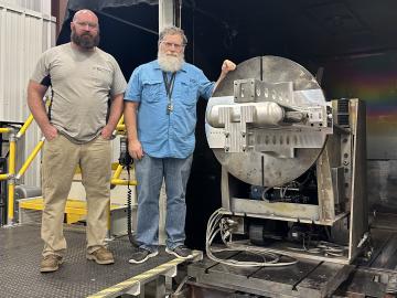 Two ORNL welders stand next to a large, round, metal electron beam welder 