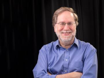 Research scientist Daniel Jacobson is standing with his arms crossed with a dark black backdrop