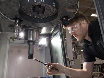 Machinist leans under machine spindle to conduct tap test with modal hammer