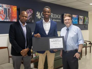 ORNL researcher Dalton Lunga and his son Langa Luna stand next to ORNL Director as he presents an award certificate to Langa (middle).