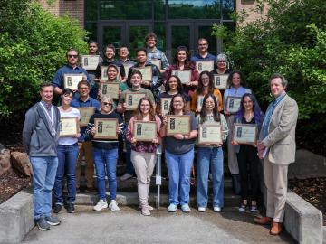 group photo taken in front of a brick building of people holding award plaques