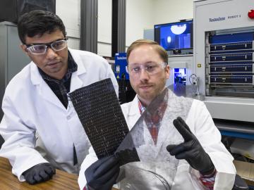 Two ORNL researchers inspect carbon fiber materials - one black rectangular sheet and one see-through sheet of film.