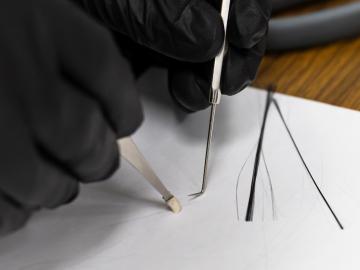 Close up image of researcher's hands showing a PAN nanofiber next to a strand of human hair.