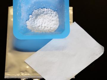 Adding powdered silica (in blue container) to the polymer layer (white sheet) that separates electrodes inside a test battery (gold bag) will prevent lithium-ion battery fires. Credit: Gabriel Veith 