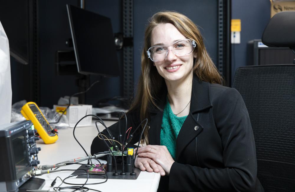 A woman sits at a desk with cybersecurity research equipment.