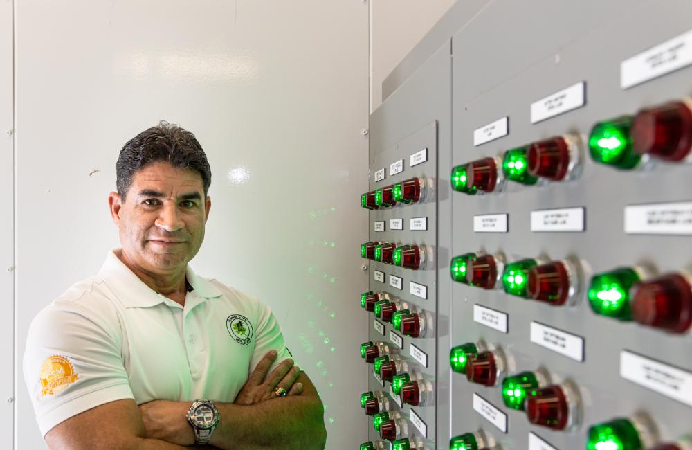 A man stands with arms crossed next to an energy system control panel