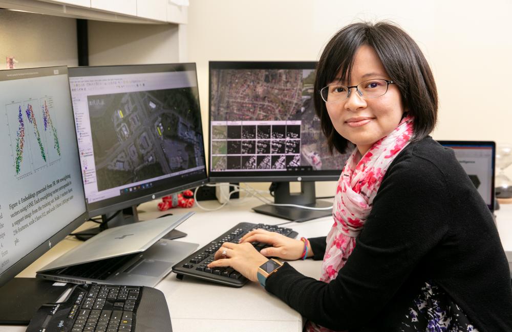 A woman works at her desk with multiple computer monitors.