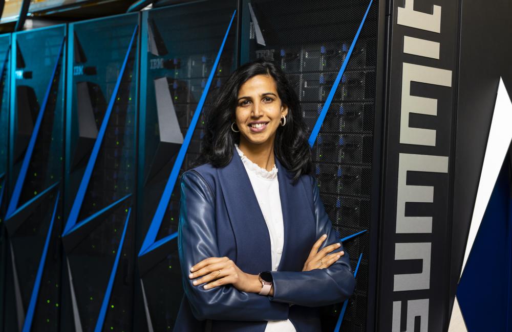 A woman stands in front of the Summit supercomputer