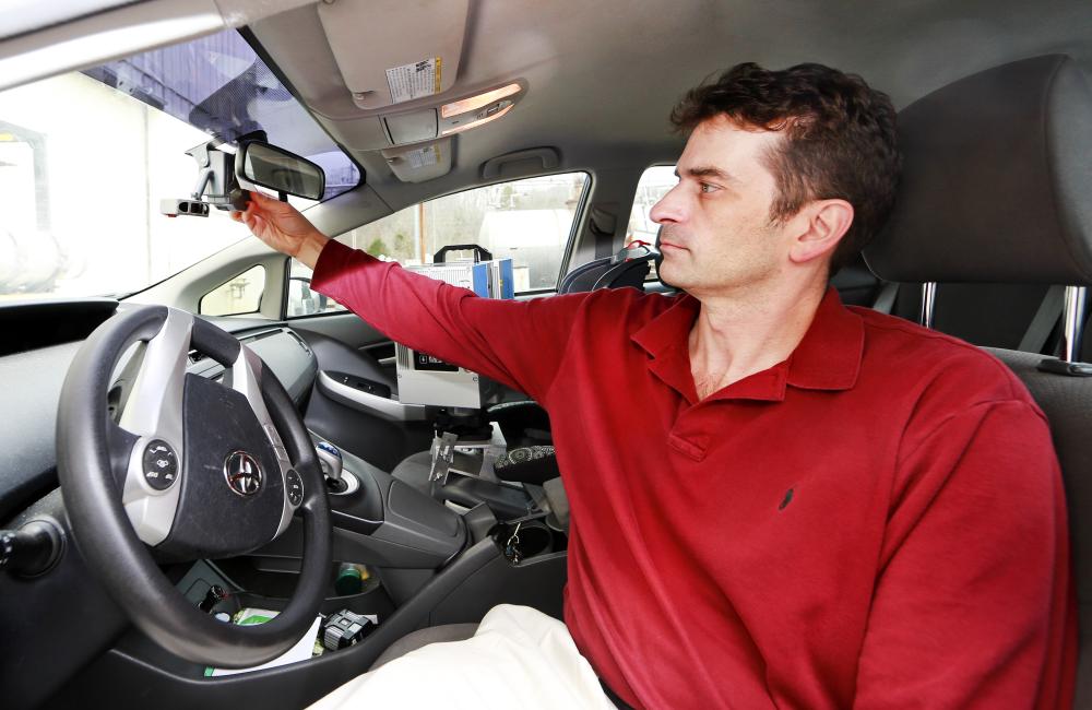 Tom Karnowski sits in the drivers seat of a car and adjusts a sensor behind the rear view mirror