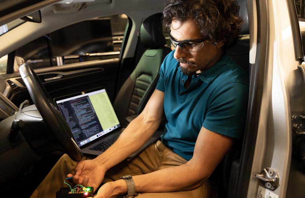 A man in a car displaying a fuse box and a computer