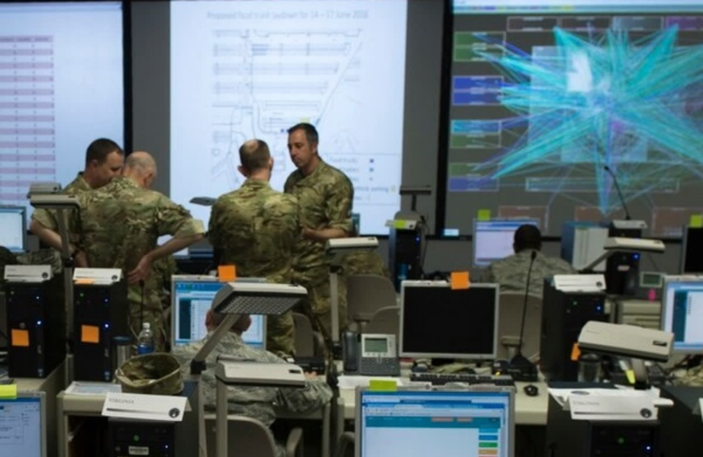 Men in military uniforms work in a room with computers and displays