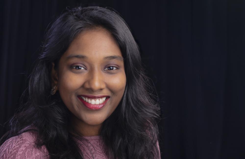 Portrait of Sreelekha Guggilam in purple shirt with black background. 