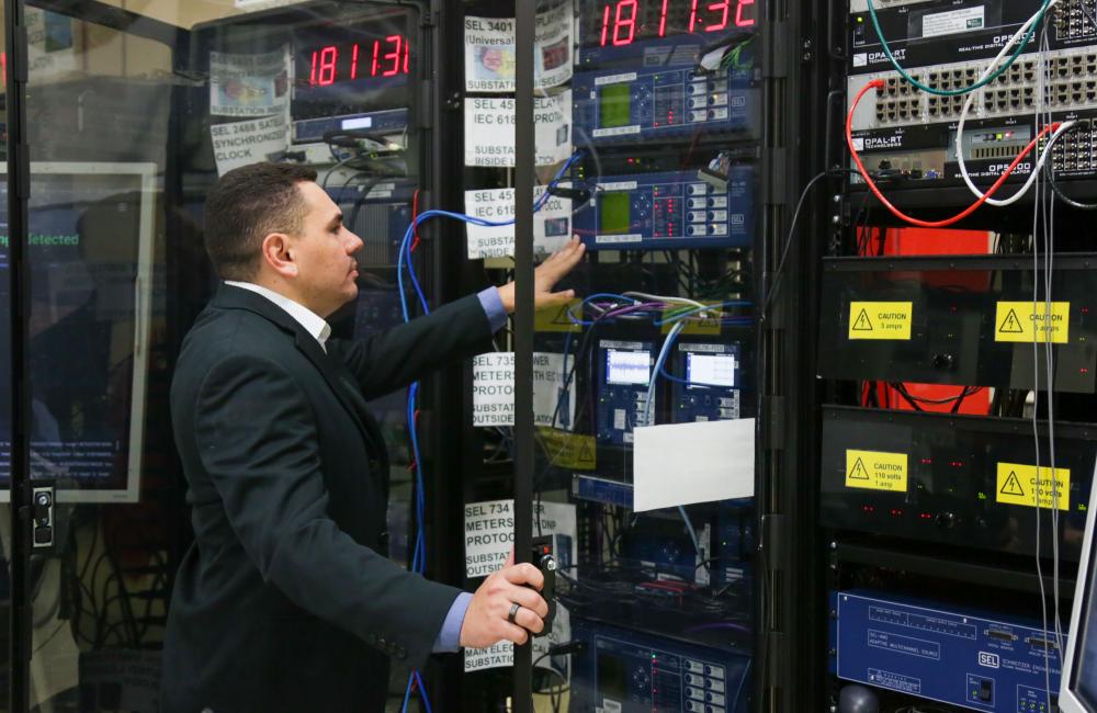 Man reaching into electrical cabinet full of meters, breakers and other power flow equipment 