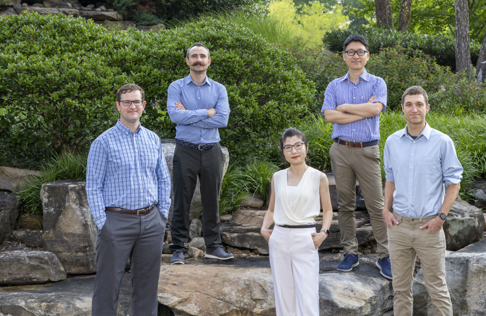 Matthew Brahlek, Jack Cahill, Eugene Dumitrescu, Takaaki Koyanagi and Dan Lu standing together on a rock structure at ORNL.