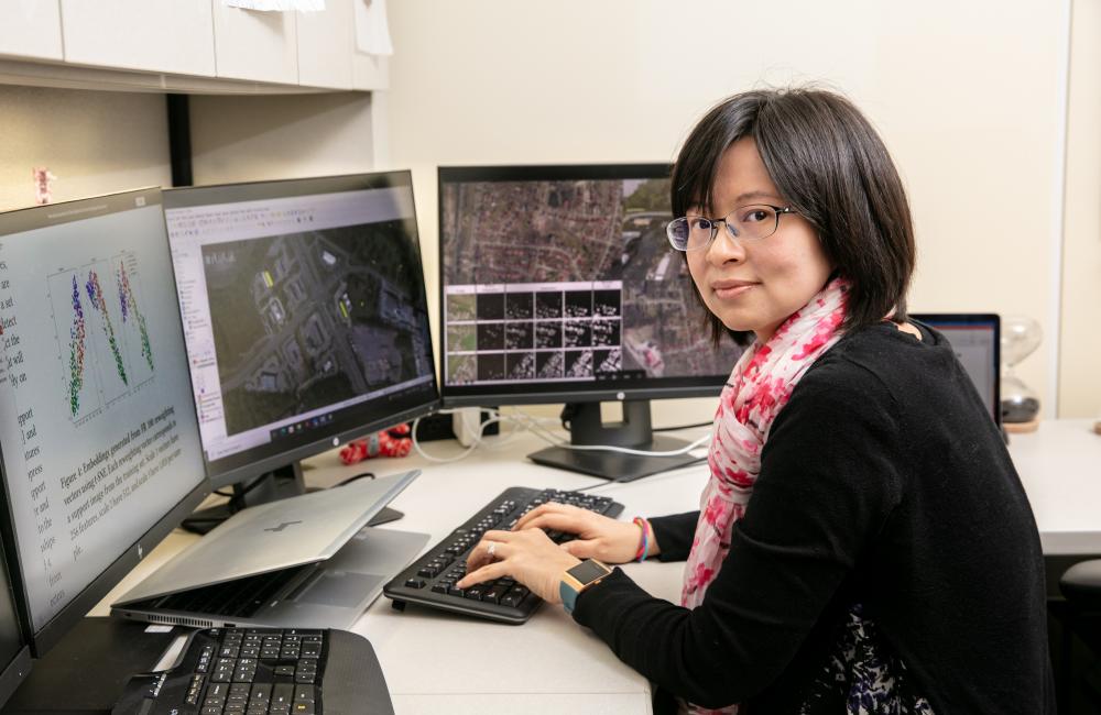 A woman sits at a computer with maps on the screen