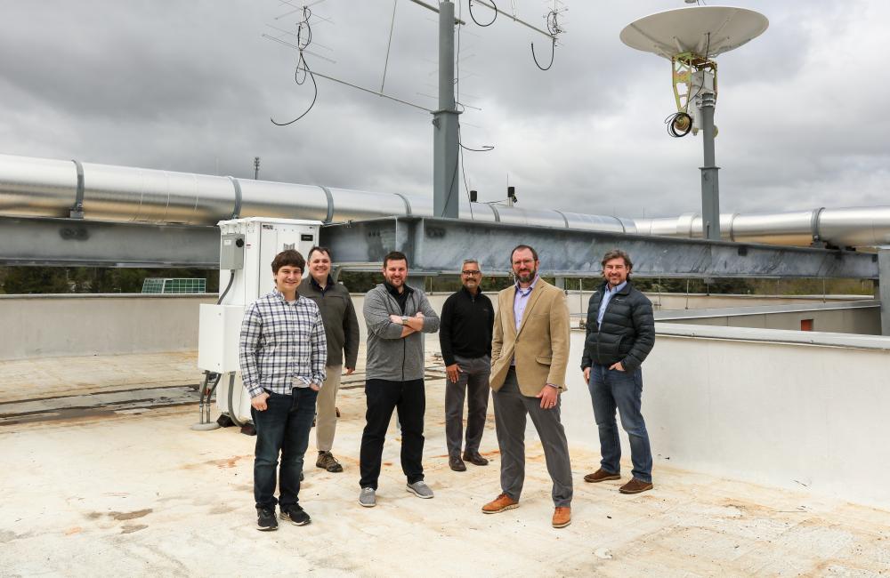 Six men stand in front of a satellite dish
