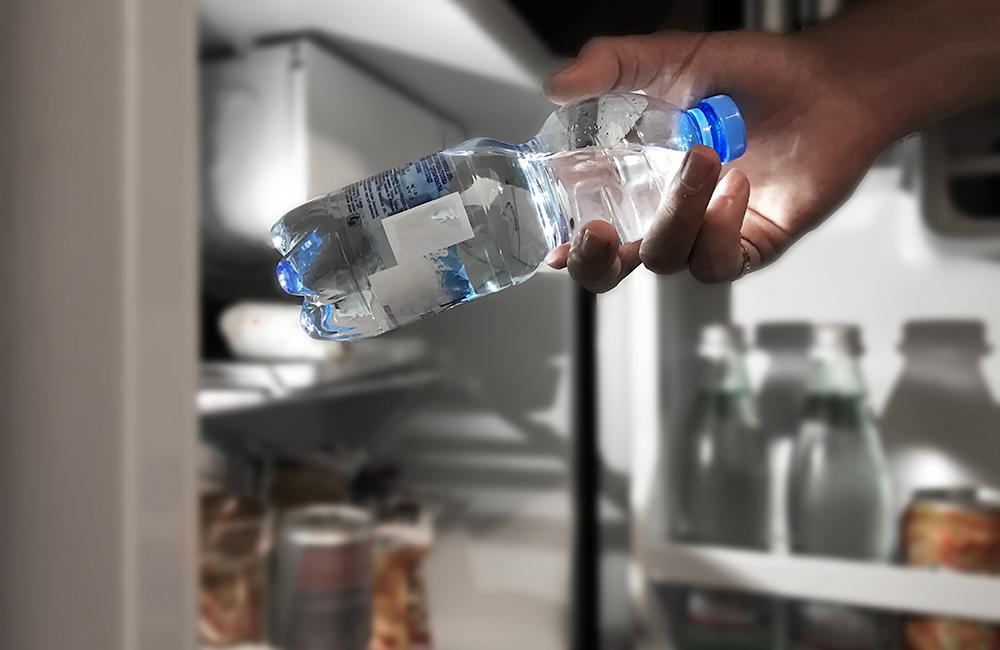 Hand holding water bottle in front of open refrigerator door