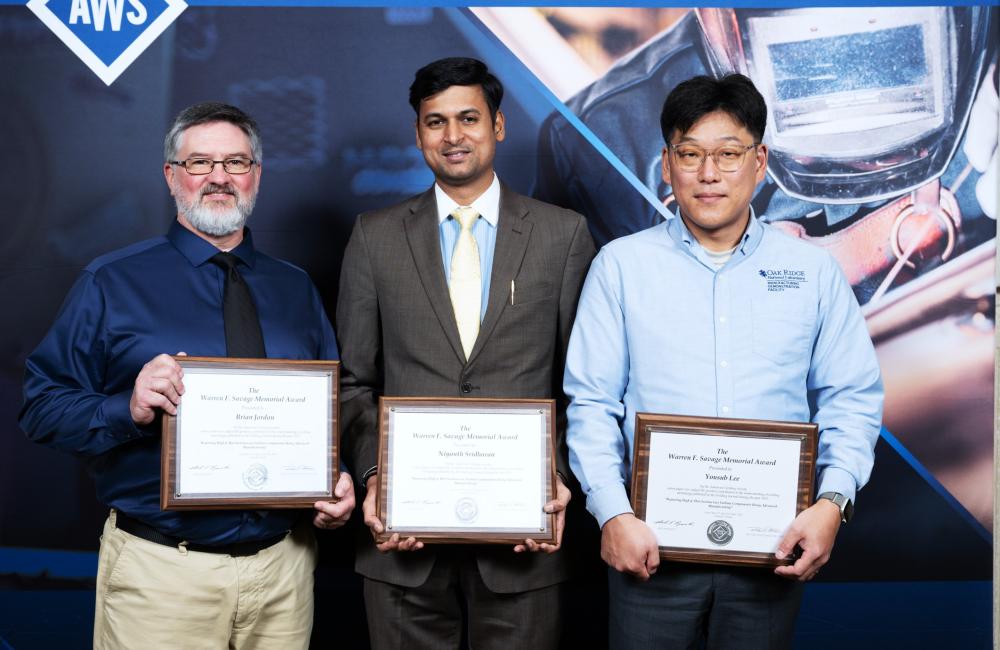 Three team members stand holding their award for bet paper by Welding Journal