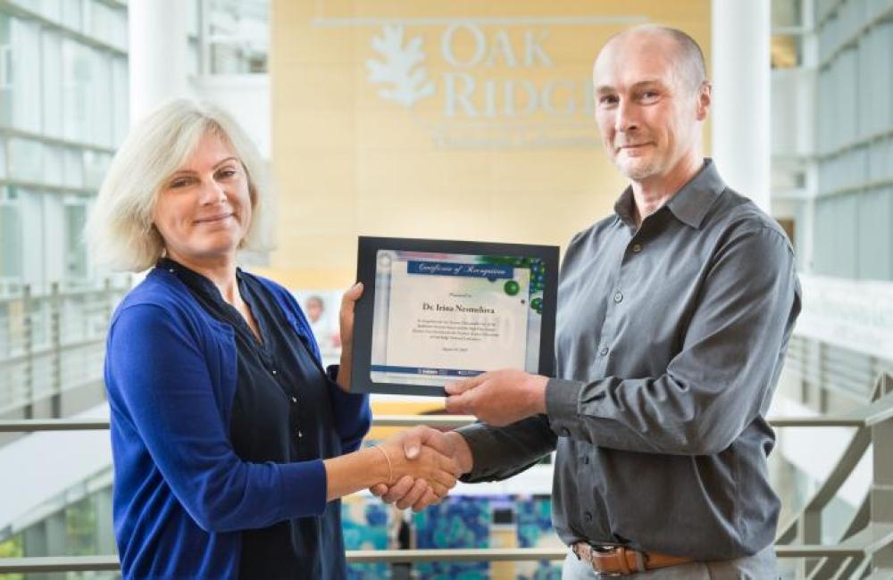 Associate Lab Director Paul Langan on the right, shaking hands and handing an award to Irina Nesmelova on the left.