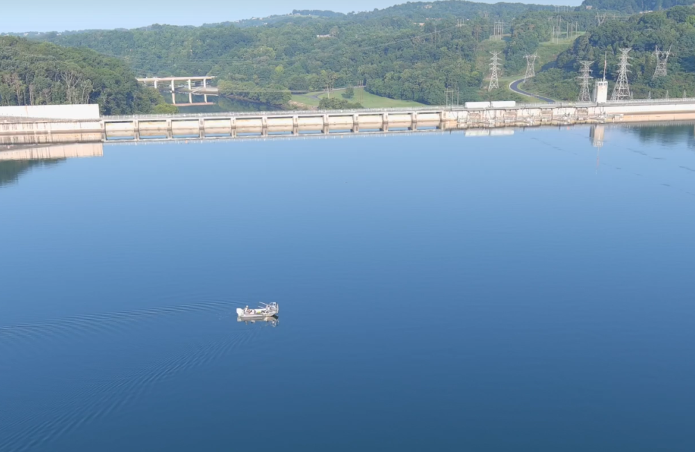researchers collect data in a lake on a boat in front of a dam
