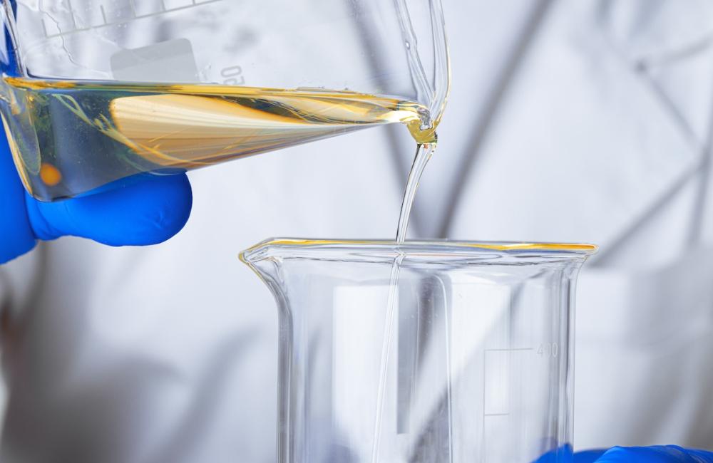 Scientist or doctor in blue gloves pouring some yellow liquid into a flask. Image from Envato