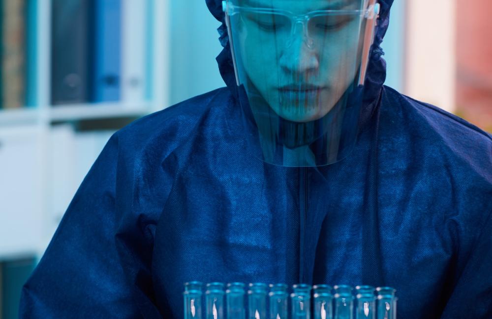 Vertical portrait of scientist in full protective costume holding test tubes while working on research in laboratory. Image from Envato