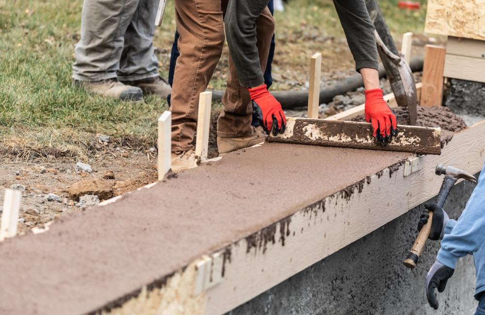 Construction Workers Pouring And Leveling Wet Cement Into Wood Framing. Image from Envato