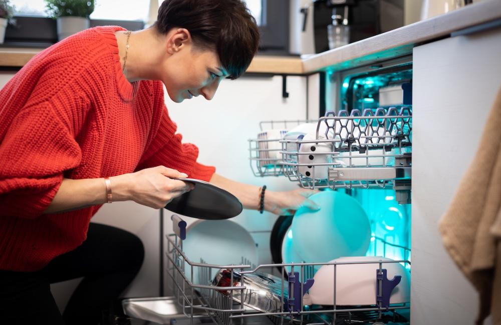 Woman putting dishes in dishwasher at white home kitchen. Image from Envato