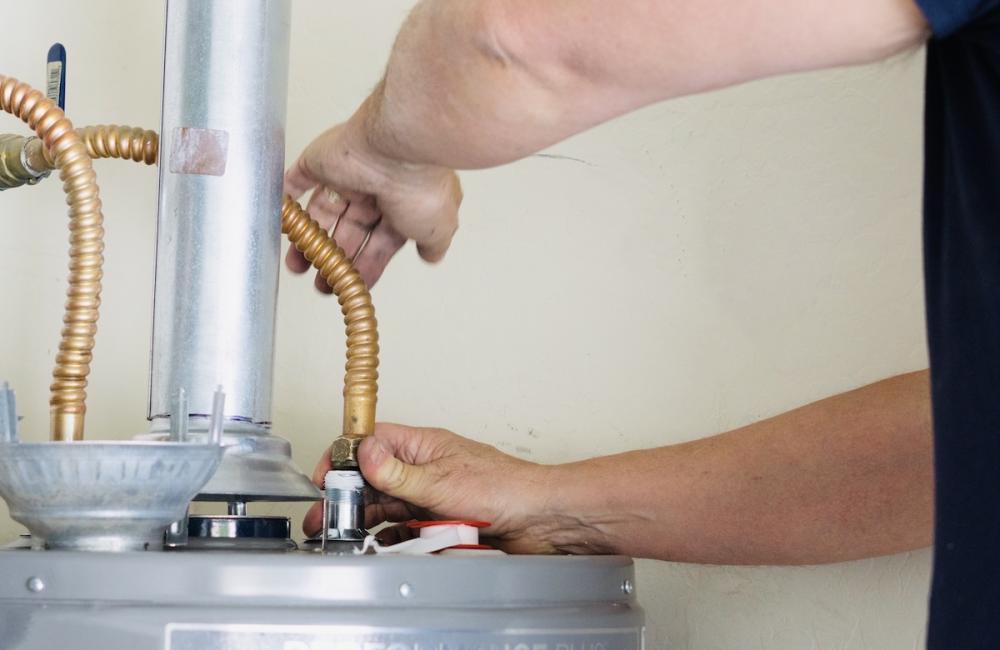 Adult male making adjustments and tightening connections on new hot water heater. Image from Envato