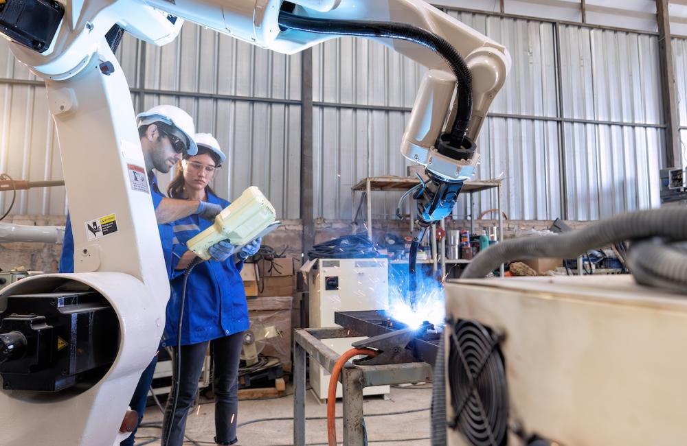In robotic maintenance shop an engineer hold controller operate robot arm welding fire spark. Image from Envato