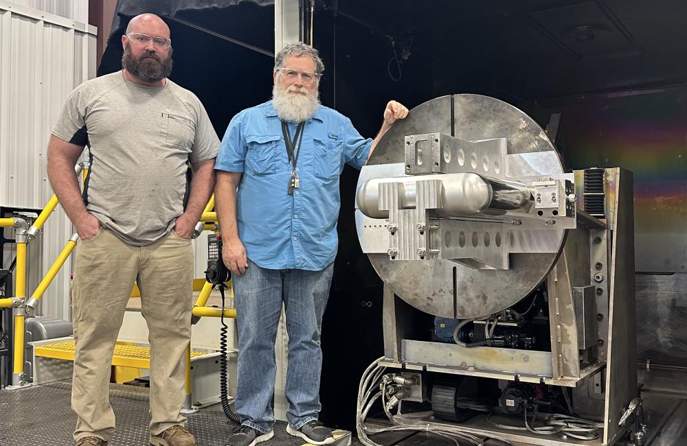 Two ORNL welders stand beside a large metallic circular welding fixture