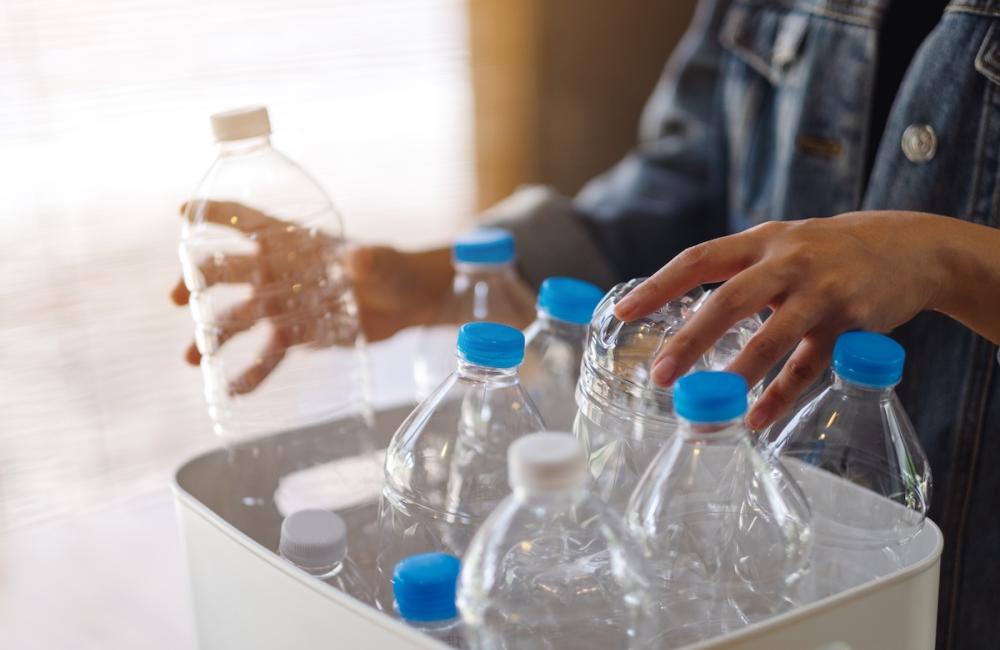 A woman collecting and separating recyclable garbage plastic bottles into a trash bin at home. Image from Envato