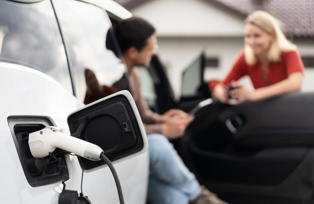 Electric car being charged while two people have a conversation. Image from Envato.