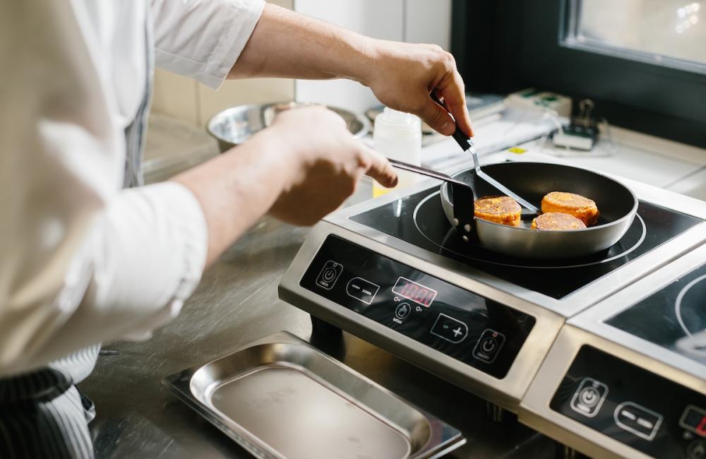 Male chef frying carrot pancakes in restaurant kitchen. Image from Envato