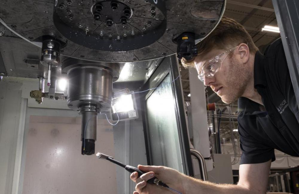 Machinist leans under machine spindle to conduct tap test with modal hammer